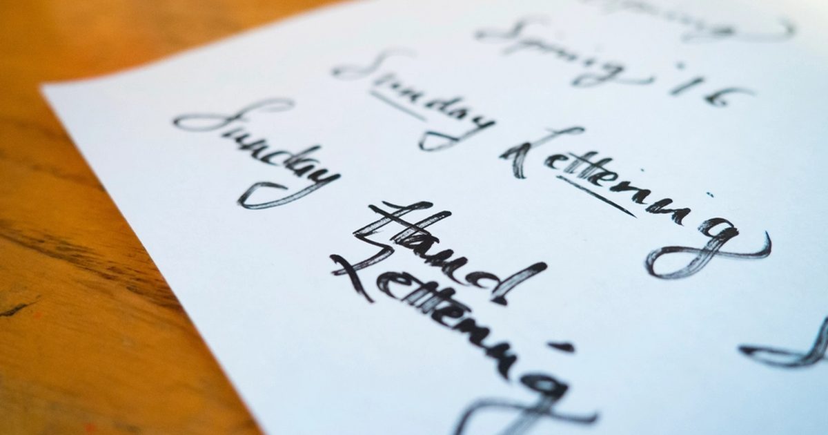 Hand lettering sketches on paper resting on a wooden desk