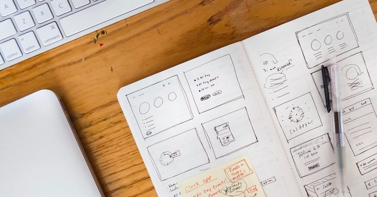 Website wireframe sketches in a notebook beside a laptop and keyboard