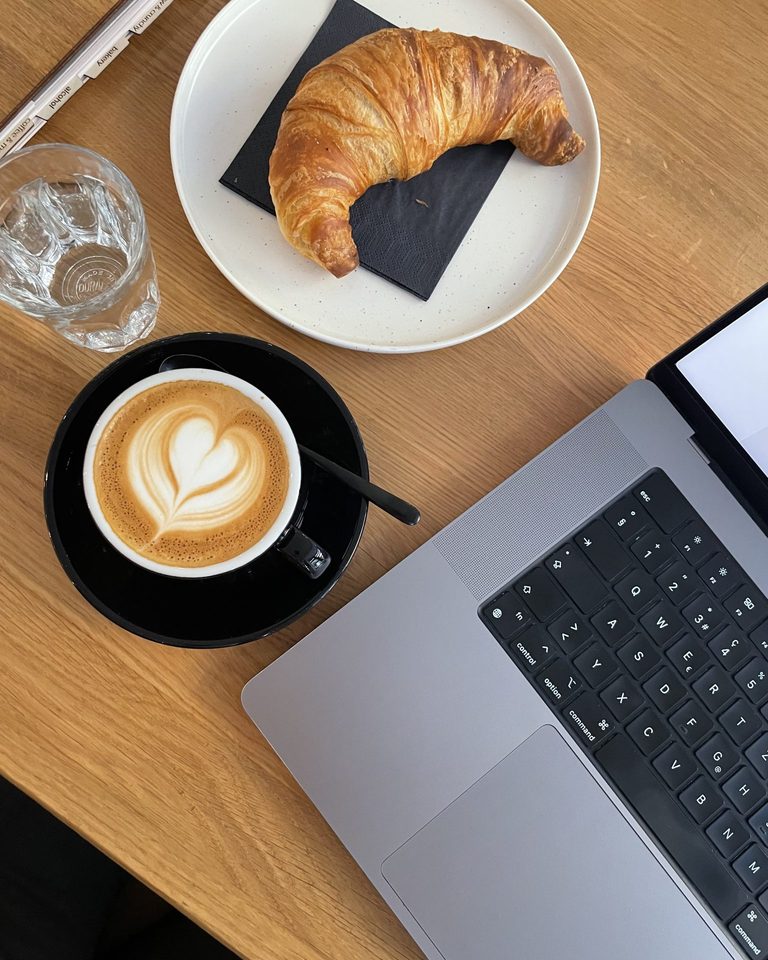 Laptop, latte, and croissant on a cafe table