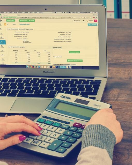 Hands working a calculator in front of a laptop spreadsheet